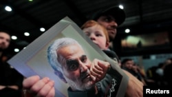 Seorang pendukung Hizbullah Lebanon menggendong seorang anak yang memegang foto mendiang komandan tertinggi Pasukan Kurdi, Qassem Soleimani, dalam pawai di pemukiman di selatan Beirut, Lebanon, 16 February 2020. (Foto: Reuters)