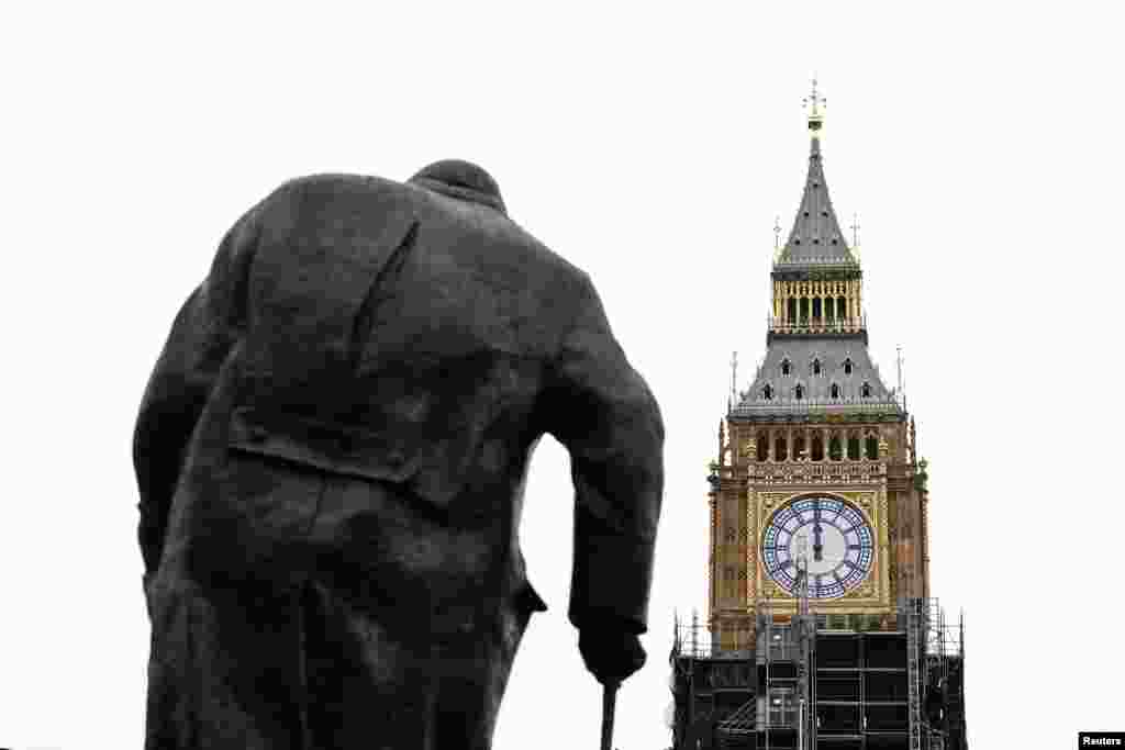 A clock face shows midday on Elizabeth Tower, more commonly known as Big Ben, with a statue of former British Prime Minister Winston Churchill in the foreground, ahead of New Year's Eve events when all four faces will be visible for the first time to ring