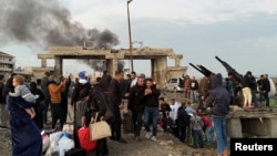 Smoke rises from the Syrian side, as people gather with belongings at the damaged site on the Lebanese-Syrian border crossing of Arida