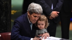 FILE - Then-U.S. Secretary of State John Kerry holding his granddaughter, Isabelle Dobbs-Higginson, signs the book during the signature ceremony for the Paris Agreement at the United Nations General Assembly Hall, April 22, 2016, in New York.