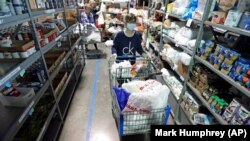 In this April 9, 2020, photo, worker Laura Burbank pushes a cart filled with food for a family through the pantry at GraceWorks Ministries food pantry in Franklin, Tenn. (AP Photo:Mark Humphrey) 