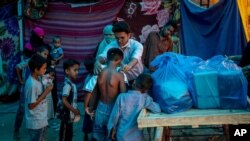 A Rohingya activist distributes new clothes among refugees at a refugee camp alongside the banks of the Yamuna River in the southeastern borders of New Delhi, sprawling Indian capital, July 1, 2021.