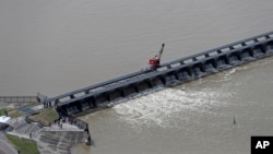 FILE - Workers open the gates of the Bonnet Carre spillway, a river diversion structure, which diverts water from the rising Mississippi River, left, to Lake Pontchartrain, in Norco, La., March 8, 2018.