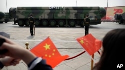 Los espectadores ondean banderas chinas mientras vehículos militares con misiles balísticos DF-41 ruedan durante un desfile en Beijing, China, el 1 de octubre de 2019.