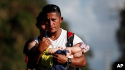 El migrante hondureño Selvin Hernández lleva a Mayra Irene, hija de otro migrante, en medio de un grupo que intentan llegar a Estados Unidos. Muchos como Hernández están siendo deportados desde México y se teme podrían haberse contagiado con el coronavirus. 