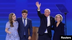 美國明尼蘇達州州長蒂姆·沃爾茲(Tim Walz，圖右二) 在接受副總統提名後與家人在講台上向在場聽衆揮手。(路透社照片)