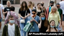 A woman sniffs a red rose as she walks, surrounded by people, some of them still in masks to protect against coronavirus, in downtown Kyiv, Ukraine, Tuesday, June 9, 2020. (AP Photo/Efrem Lukatsky)