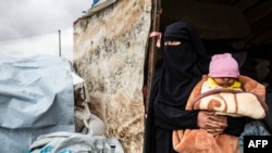 Seorang perempuan sedang menggendong bayi melihat keluar dari tenda saat dia mengemasi barang-barangnya sebelum meninggalkan kamp al-Hol di Provinsi al-Hasakeh di timur laut Suriah, 16 November 2020 (Foto: AFP)