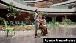 ក្មេង​ប្រុស​ម្នាក់ ឈរ​ជាមួយ​សមាជិក​គ្រួសារ​នៅ​ក្នុង​កន្លែង​ចាក់​វ៉ាក់សាំង Discovery ខណៈ​ដែល​ខ្លួន​រង់ចាំ​ចាក់​វ៉ាក់សាំង Pfizer/BioNTech ដូស​ដំបូង​នៅ​តំបន់ Sandton នៃ​ប្រទេស​អាហ្វ្រិក​ខាងត្បូង នៅ​ថ្ងៃទី១៥ ខែធ្នូ ឆ្នាំ២០២១។