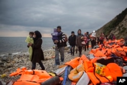 FILE - Refugees and migrants walk along a beach after crossing a part of the Aegean on a dinghy, from Turkey to the Greek island of Lesbos, Dec. 12, 2015.