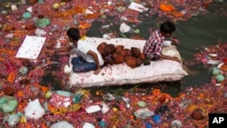 Indian children sit on a makeshift raft as they search for reusable items among offerings thrown by devotees in river Sabarmati at the end of Dashama festival in Ahmadabad, India, Monday, Aug. 24, 2015.