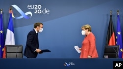 German Chancellor Angela Merkel, right, and French President Emmanuel Macron prepare to address a media conference at the end of an EU summit in Brussels, Tuesday, July 21, 2020. Weary European Union leaders finally clinched an unprecedented budget 