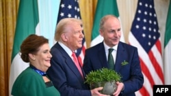 US President Donald Trump and Irish Prime Minister Micheal Martin (R) hold a bowl of shamrock alongside his wife Mary O'Shea (L) during a St. Patrick's Day Reception in the East Room of the White House in Washington, DC, on March 12, 2025. (Photo by Mande