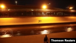 ARCHIVO - Migrantes en la orilla del Río Bravo luego de cruzarlo para entregarse a agentes de la Patrulla Fronteriza de EE. UU. para pedir asilo en El Paso, Texas, mientras un soldado de la Guardia Nacional Mexicana patrulla la frontera en Ciudad Juárez.