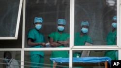 In this March 5, 2021, file photo, medical staff look out from a window as officials prepare for a ceremony to commence the country's first coronavirus vaccinations using AstraZeneca provided through the global COVAX initiative, at Kenyatta National Hospi