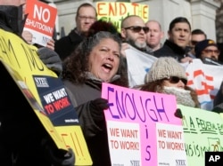Internal Revenue Service employee Mary Maldonado, of Dracut, Mass., center, displays a placard during a rally by federal employees and supporters, Jan. 17, 2019, in front of the Statehouse, in Boston, held to call for an end of the partial shutdown.