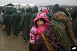 A migrant holds her child as she queues for food portions at the Greek border camp near Idomeni, March 10, 2016.