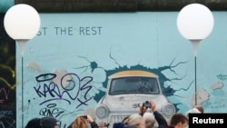 (រូបភាព​ឯកសារ)​ មនុស្ស​ដើរកាត់​ និងថត​រូបភាព​ក្បែរ​កន្លែង​តាំង​'Lichtgrenze' ព្រំដែន​នៃពន្លឺ តាម​បណ្តោយ​សាល​កម្រង​រូបភាព​ផ្នែកខាង​កើត ដែល​ជាតំបន់​មាន​ផ្នែក​ជញ្ជាំង​បែរឡាំង​ធំជាងគេ​បង្អស់​សេសសល់​ ក្នុងរដ្ឋធានី​បែរឡាំង​ ប្រទេស​អាល្លឺម៉ង់​ ថ្ងៃទី៩​ ខែ​វិច្ឆិកា ឆ្នាំ​២០១៤។ 