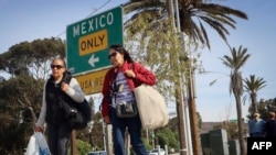 FILE - Shoppers walk with their purchases near the U.S.-Mexico border in San Ysidro, California, on Nov. 26, 2024.
