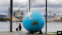 Ljudi prolaze pored skulpture zemaljske kugle u Thea's parku u Tacomi u državi Washington, a u pozadini je tvornica papira WestRock.