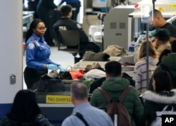 Los agentes de la Administración de Seguridad en el Transporte ayudan a los pasajeros a través de un punto de control de seguridad en el Aeropuerto Internacional Newark Liberty en Newark, N.J., el lunes 7 de enero de 2019.