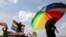 FILE - A person holds an umbrella bearing the colors of the rainbow flag as others wave flags during a gay pride rally in Entebbe, Uganda, Aug. 9, 2014. A crowd in Ghana tore down a billboard promoting LGBTQ tolerance in June 2022, during Pride month.