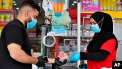 In this Saturday, May, 2, 2020, photo, a man uses banknotes to pay for his purchases at the mall in Basra, Iraq. The coronavirus pandemic has renewed debate about the use of paper money and coins. (AP Photo/Nabil al-Jurani)