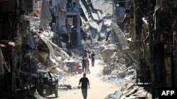 Палестинци поминуваат по тесна улица покрај уништените згради во Кан Јунис, во јужниот дел на појасот Газа на 11 јуни 2024 година, среде тековниот конфликт меѓу Израел и палестинската милитантна група Хамас (Фото: АФП)
