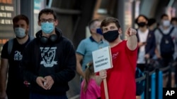 A staff member carries a sign looking for passenger from high-risk-countries at a Corona test center at the airport in Frankfurt, Germany, Friday, Aug. 7, 2020. Sign reads "home comers from high-risk-countries" .(AP Photo/Michael Probst)