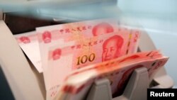 FILE - Chinese 100 yuan banknotes are seen in a counting machine while a clerk counts them at a branch of a commercial bank in Beijing, China, March 30, 2016. 