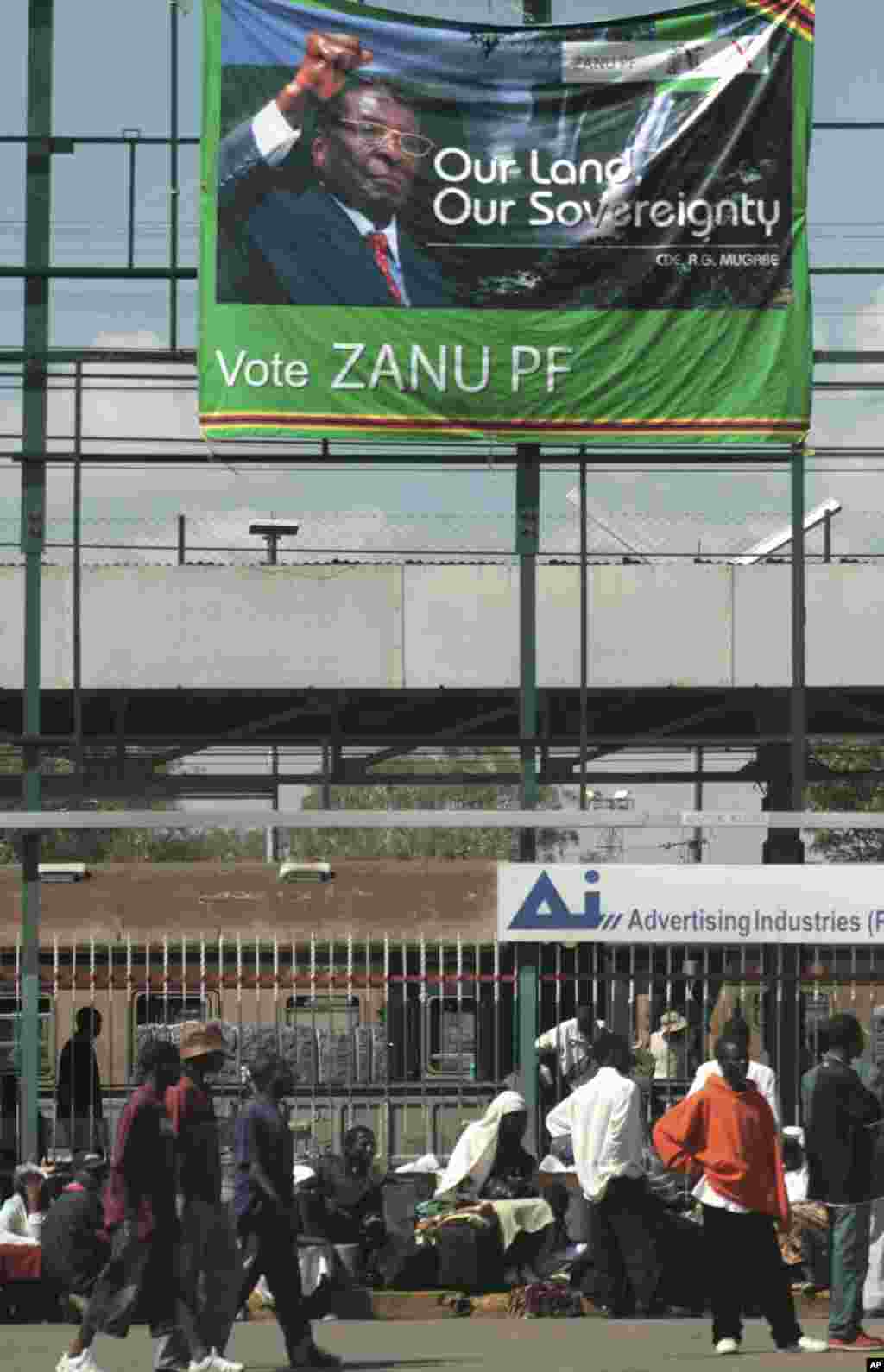 Pedestrians pass beneath an election banner with a portrait of Zimbabwe's President Robert Mugabe in Harare Tuesday April 15, 2008. Additional police and soldiers were deployed across Zimbabwe's capital Tuesday as the country's opposition urged Zimbabweans to join in a nationwide strike to press for the released of long-delayed presidential results.