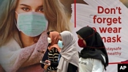 Perempuan mengenakan masker melewati poster promosi kesadaran pandemi Covid-19 di sebuah pusat perbelanjaan di Jakarta, 1 Juli 2020. (Foto: dok).