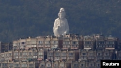 A 76-meter-high (249-feet) bronze-forged white Buddhist Avalokitesvara or Guan Yin statue, part of the Tsz Shan Monastery, stands behind luxurious houses at Taipo district in Hong Kong April 16, 2015. 