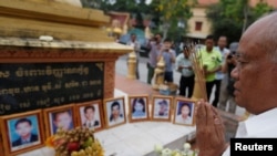 FILE - A man prays in front of portraits of victims of a fatal 1997 grenade attack on an opposition rally, which are displayed during a ceremony to remember the victims, at a monument in Phnom Penh, Cambodia, March 30, 2018. (Reuters)