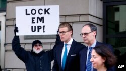 Alex van der Zwaan, centro, a su salida de la Corte Federal del Distrito en Washington, DC tras recibir su sentencia. Un residente sostiene un cartel donde se lee "enciérrelos".