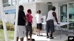 In this April 8, 2020 photo, restaurant worker Glen Pile, left, waits in line to get an unemployment form at a Miami-Dade County library during the coronavirus pandemic in Miami.