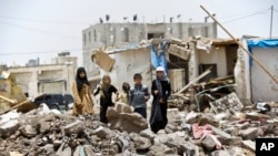 FILE - A boy and his sisters watch graffiti artists spray on a wall, commemorating the victims who were killed in Saudi-led coalition airstrikes in Yemen, May 18, 2015. 