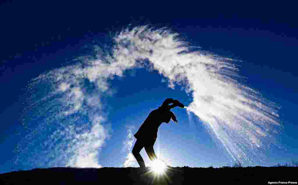 A woman throws hot water from a thermos bottle into the cold air making its three phases visible - liquid, gas, solid - as the smallest droplets cool and evaporate in a dramatic cloud before they reach the ground as snow, in Berlin on a sunny but frosty Boxing Day.