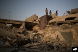 In this July 13, 2017 photo, members of a family stand on the roof of their damaged house in the west side of Mosul, Iraq.