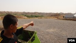 Faisel, 13, points at his house on the other side of the barbed-wire fence surrounding the camp, May 29, 2018, in Hassan Sham, Iraqi Kurdistan. (H. Murdock/VOA)