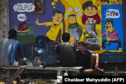 Orang-orang duduk di depan mural kampanye pemilihan umum Indonesia menjelang pemilihan bulan depan di Banda Aceh, Aceh pada 17 Maret 2019. (Foto: AFP/Chaideer Mahyuddin)