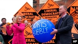 Newly elected Liberal Democrat lawmaker Helen Morgan, left, bursts a "Boris' bubble" held by colleague Tim Farron, as she celebrates in Oswestry, Shropshire, England, Dec. 17, 2021.