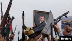 FILE - A poster of Houthi leader Abdul-Malek al-Houthi is held by a protester as others hold up their weapons during a rally to show support to Palestinians in the Gaza Strip, amid the Israel-Hamas conflict, in Sanaa, Yemen, July 26, 2024. 