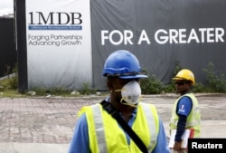FILE - Construction workers stand in front of a 1Malaysia Development Berhad (1MDB) billboard at the Tun Razak Exchange development in Kuala Lumpur, Malaysia, Feb. 3, 2016.