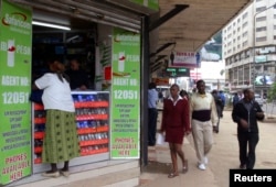 FILE - Pedestrians walk past an M-Pesa shop in downtown Nairobi, Kenya, May 12, 2009.