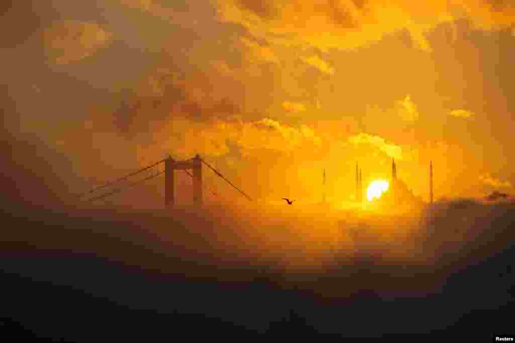The sun rises behind the Grand Camlica Mosque as July 15 Martyrs' Bridge, known as the Bosphorus Bridge, and the Bosphorus are covered in fog in Istanbul, Turkey.