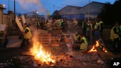 Demonstrators stand in front of a makeshift barricade set up by the so-called yellow jackets to block the entrance of a fuel depot in Le Mans, western France, Tuesday, Dec. 5, 2018. (AP Photo/David Vincent)