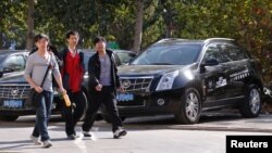 People walk past Cadillac cars outside a dealership in Beijing