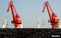 FILE - Piles of steel pipes to be exported are seen in front of cranes at a port in Lianyungang, Jiangsu province, March 7, 2015.