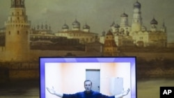 Russian opposition leader Alexei Navalny appears on a TV screen during a live session with the court during a hearing of his appeal in a court in Moscow, Russia, Thursday, Jan. 28, 2021, with an image of the Moscow Kremlin in the background. 